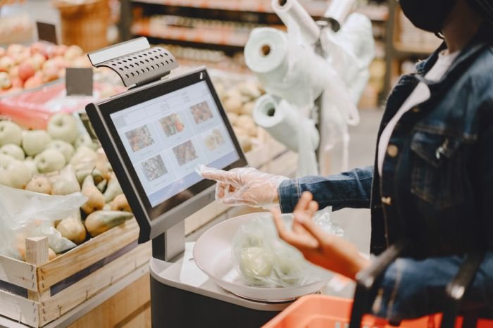 Shopper using a self-checkout kiosk to weigh and scan produce in a grocery store.